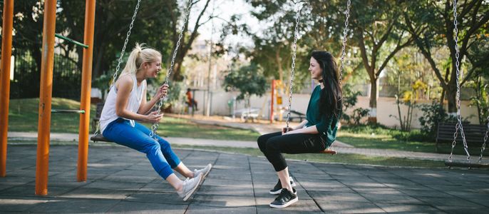 Two people talking while sitting on swings