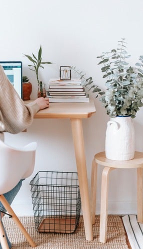 Person sitting at desk working on computer, plants and stack of books nearby